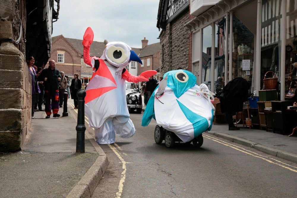 The artists are dressed as the cartoonish London Olympics mascots. They are moving through the streets.