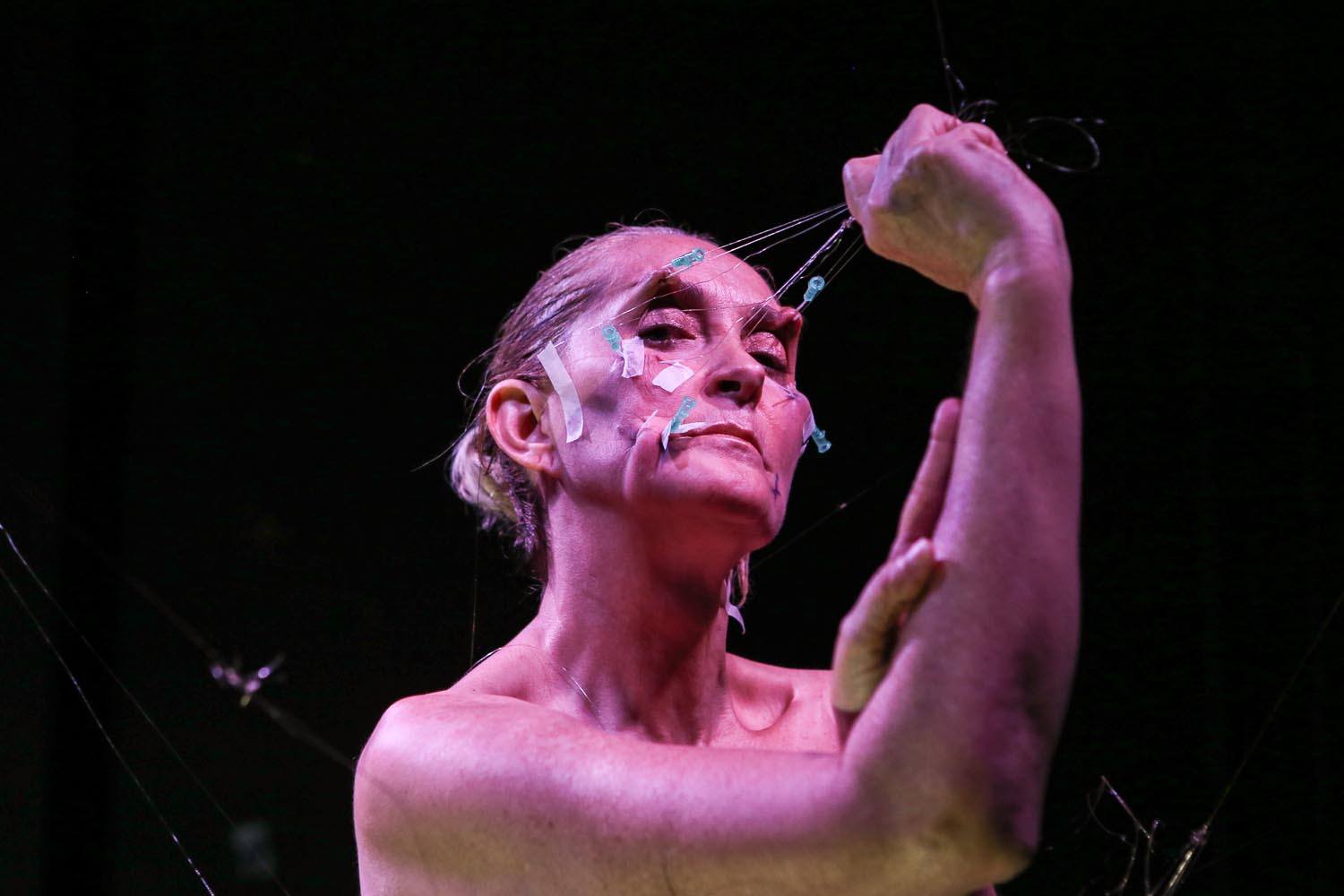 The artist pulls on wire attached to hooked needles in her face, stretching the skin.