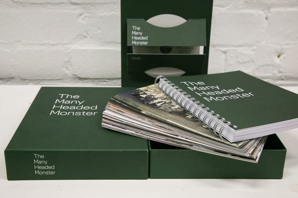 Photograph of the publication 'The Many Headed Monster', which takes the form of a box set containing numerous items. The cover is green, and the items contained within the set are stacked up on the box.