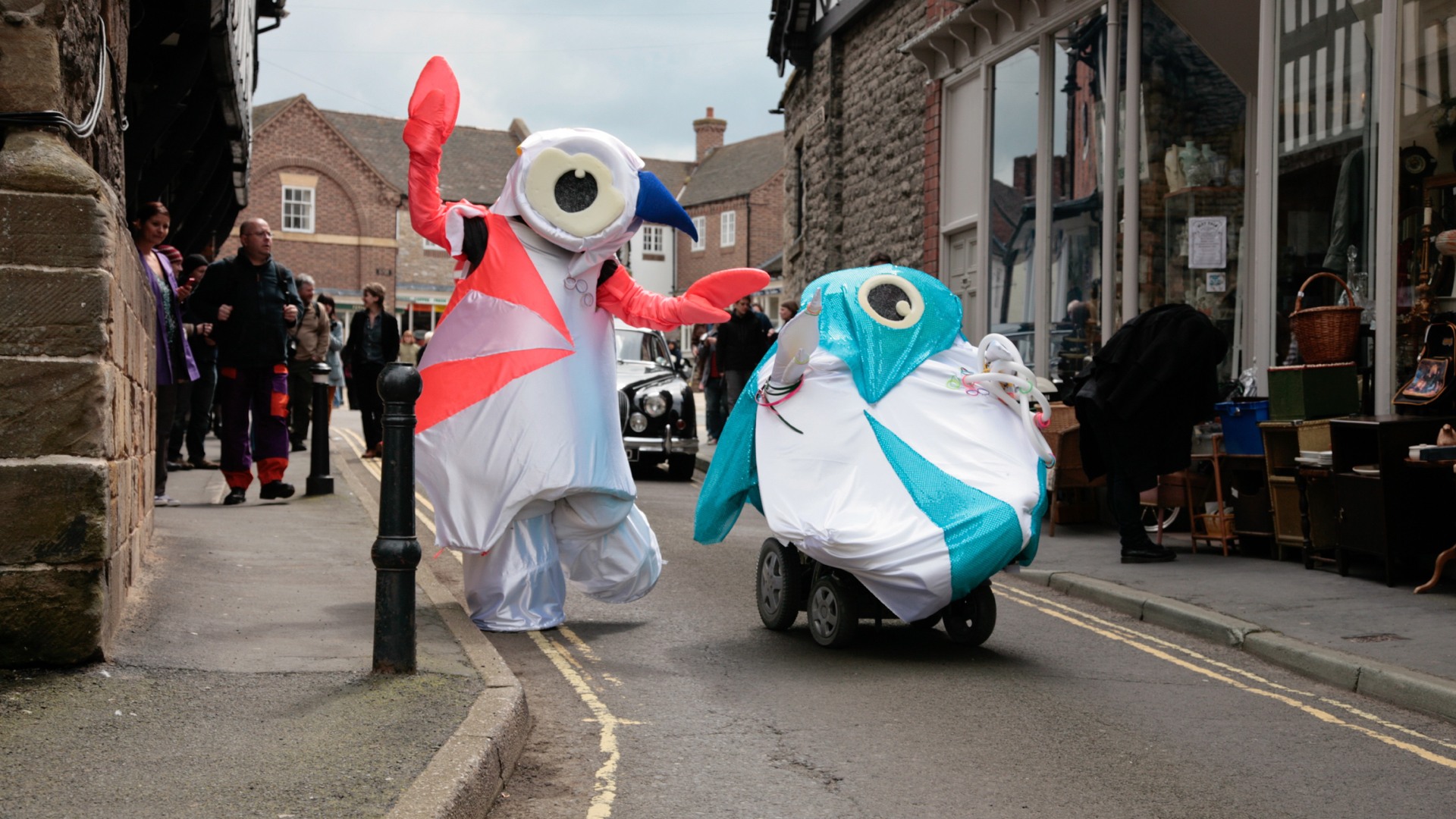 The artists are dressed as the cartoonish London Olympics mascots. They are moving through the streets.