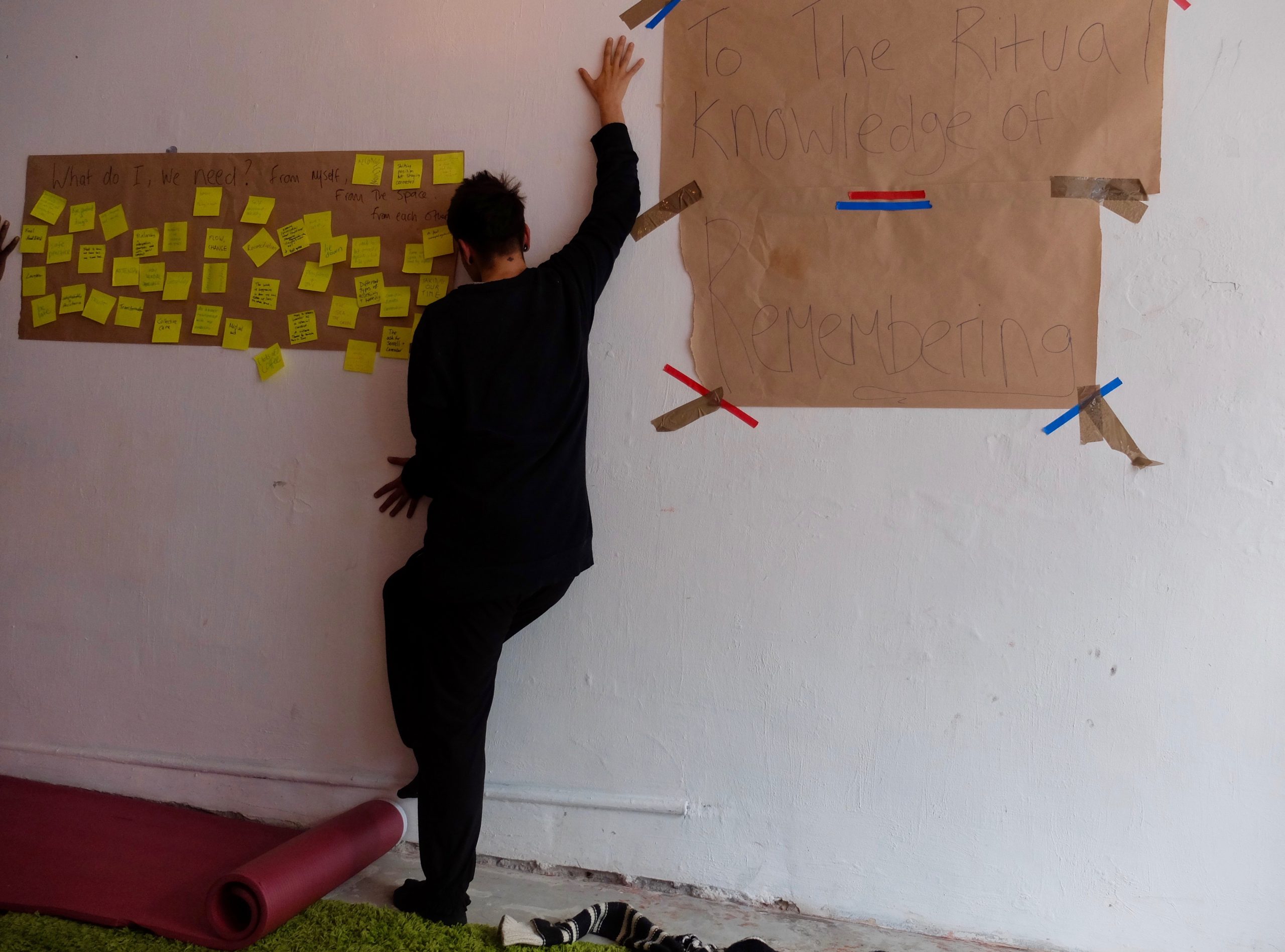 A workshop participant presses their body against a wall. Attached to the wall are various post it notes and paper sheets.