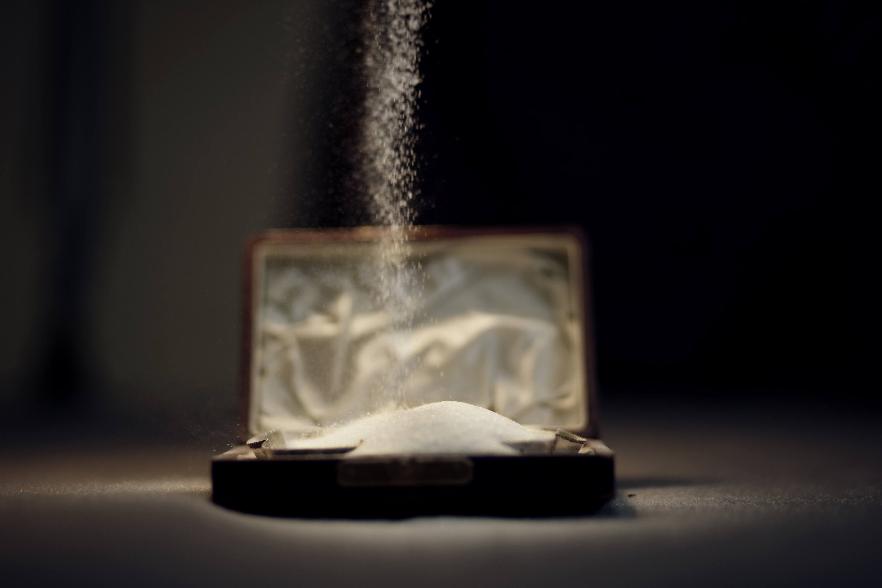 Photo of a line of salt falling down and forming a small salt mountain inside a box.