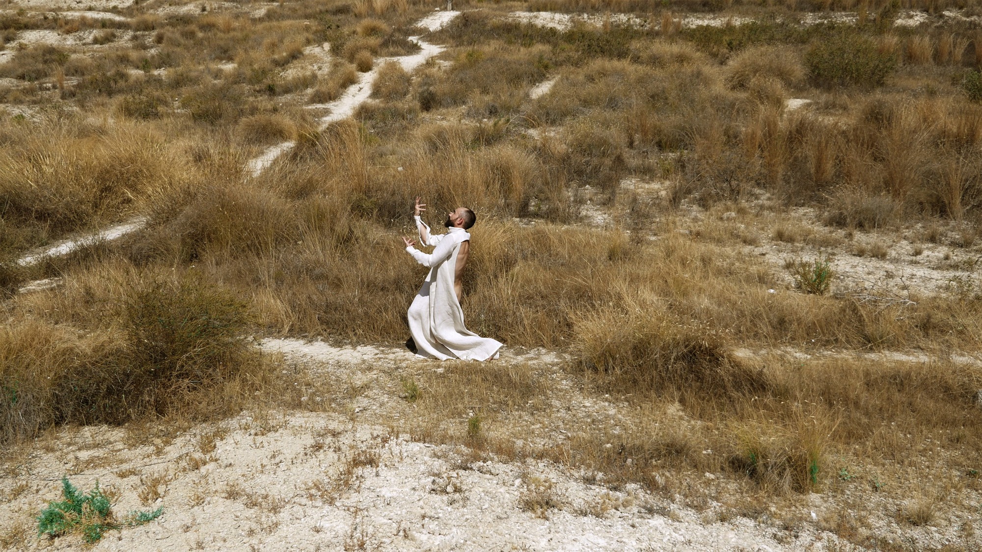 A man dances in the desert wearing a robe.