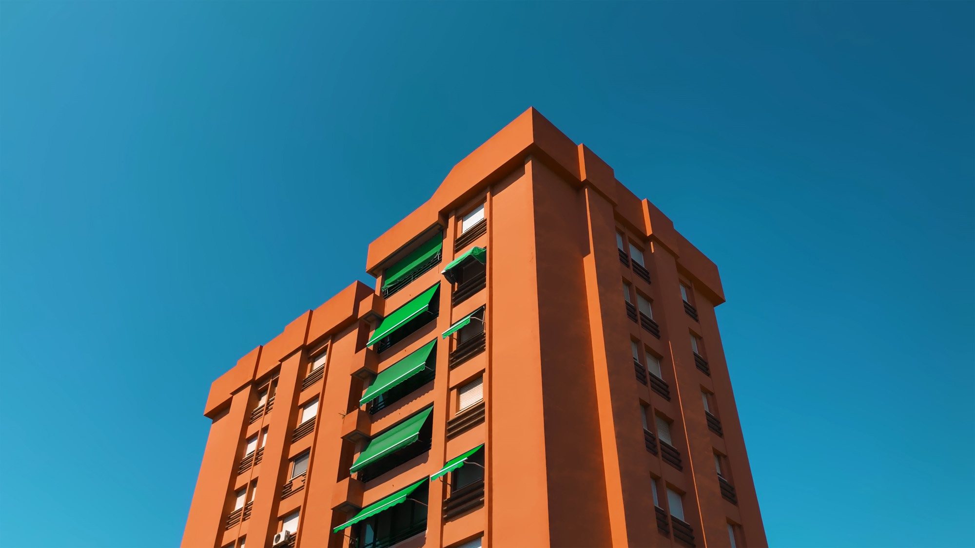 A orange tower block is shot from below, against a blue sky.