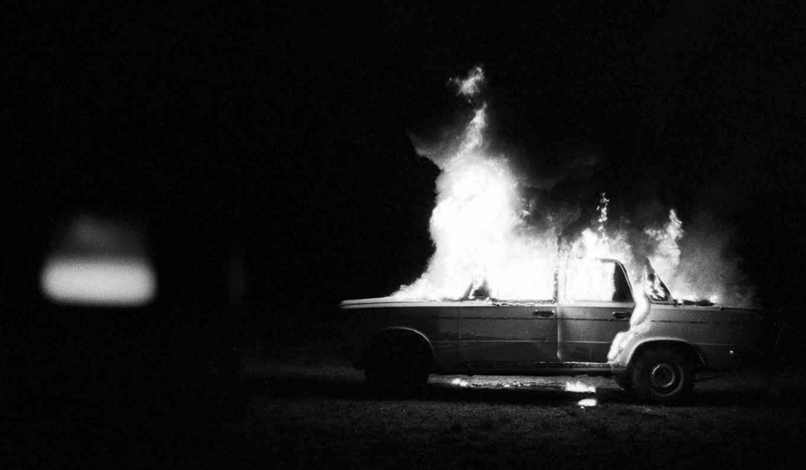 Black and white photo of a car in flames.