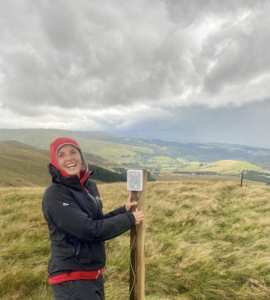 Miranda Whall stood in a field smiling, next to soil sensor technology