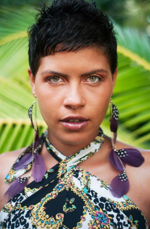 Ria Righteous stood in a tropical garden wearing a colourful floral dress and purple floral earrings