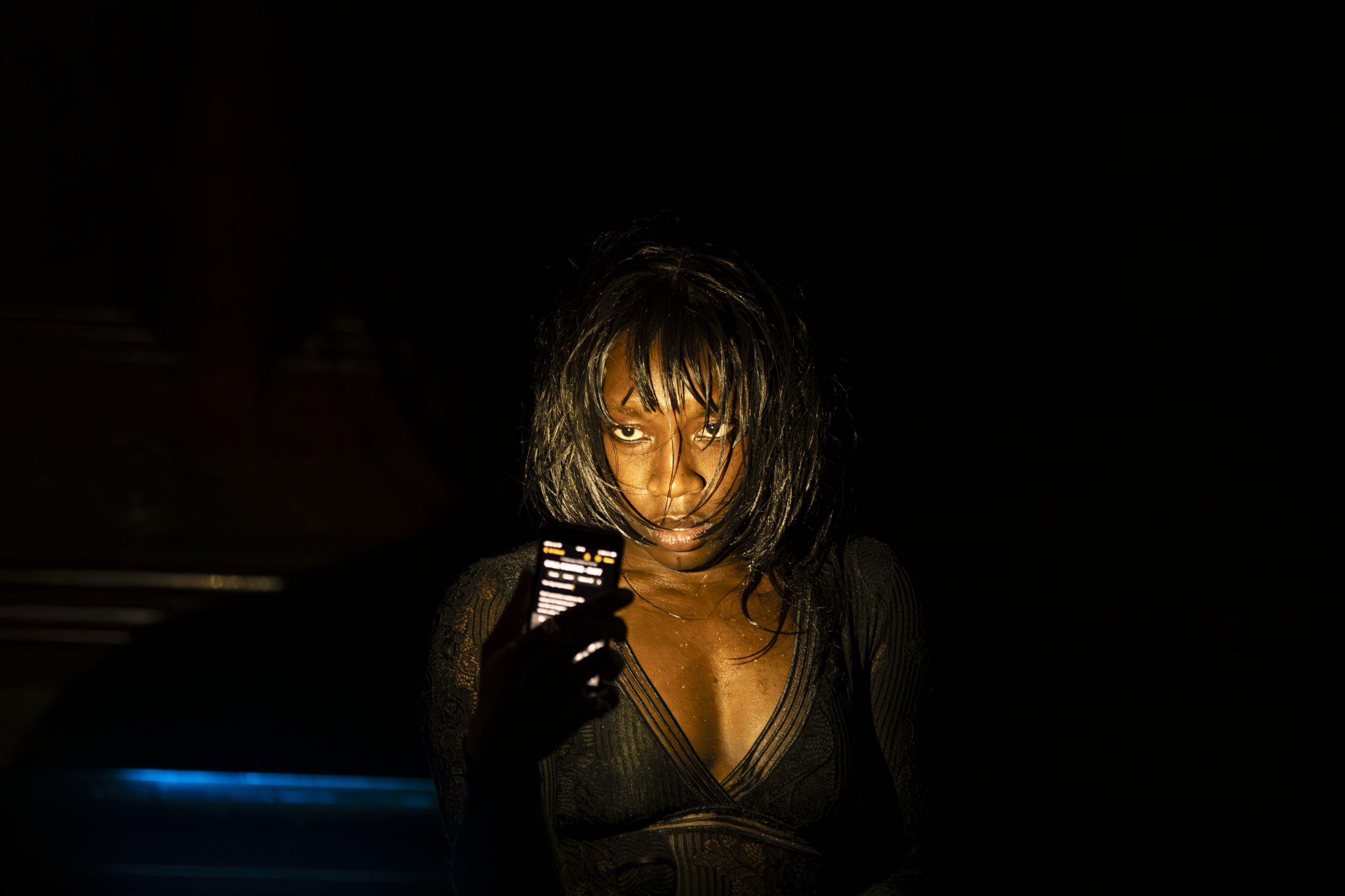 A young black woman looks into a phone camera light, their straight bob is soaking wet.