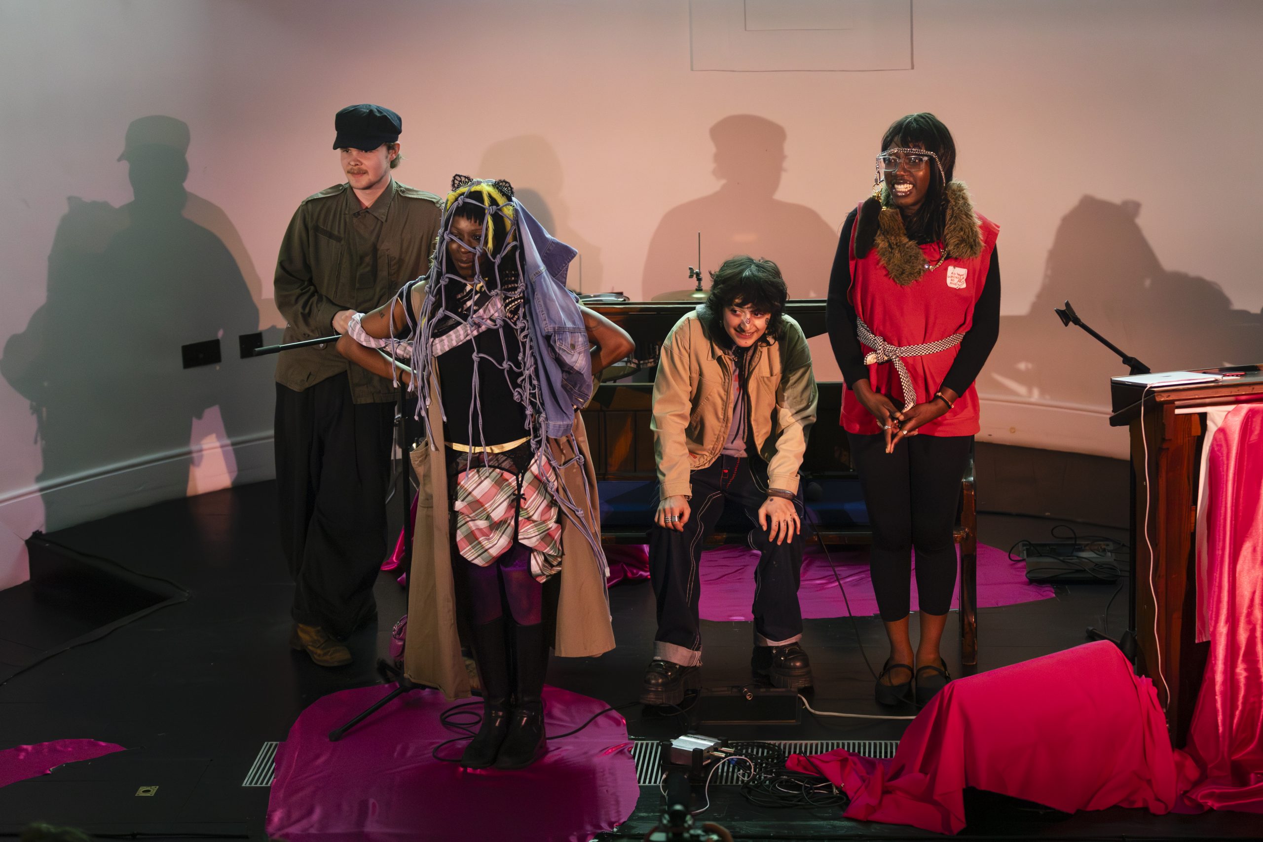 A group of four people stand on a stage, two have been dressed up in Indie Sleaze fashion.