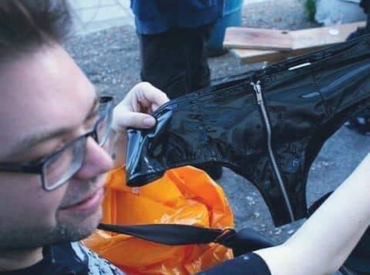 Photo of a white man holding a vinyl thong with a zipper at the crotch above a Sainsbury's bag.