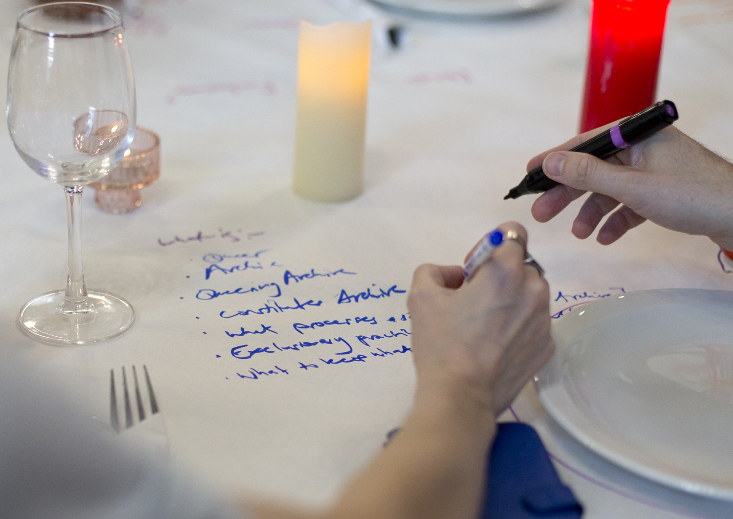 Two people writing notes with felt pens on a paper table cloth.